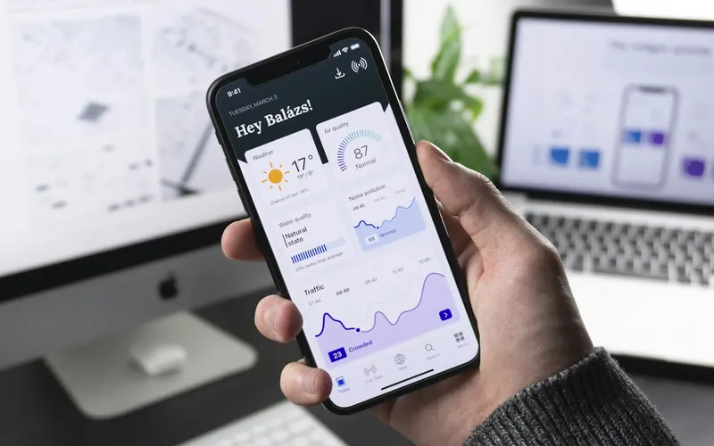 Web and mobile app development — mobile app interface in hand with web UI designs on desktop screens